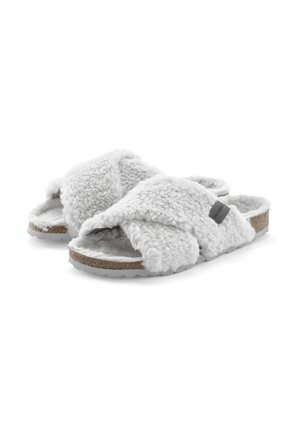 Crossed slide slippers in soft gray faux fur, featuring a cork sole. The design includes plush texture and a low-profile heel for comfort.