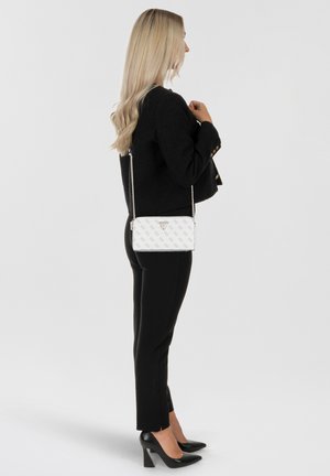 Weißes Leder-Crossbody-Bag mit einem gemusterten Design, silberner Kettenriemen, dreieckigem Logo-Akzent, getragen von einer Person in schwarzer Kleidung.