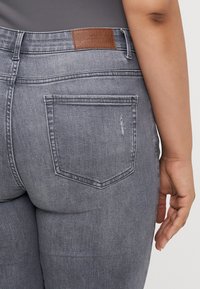 Gray denim jeans featuring a leather patch on the waistband, back pockets, and subtle distressed detailing. Fitted design with smooth texture.