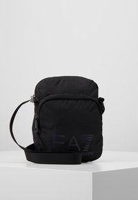Borsa a tracolla nera in nylon con chiusura a zip, tracolla regolabile e logo EA7 inciso sul davanti. Design compatto con texture liscia.
