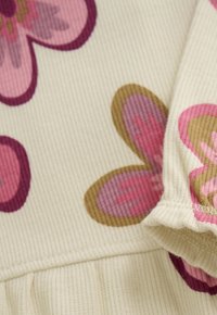 Nahaufnahme von cremefarbenem geripptem Stoff mit rosa und braunen Blumenmustern sowie detaillierter Naht an einer gefalteten Kante.