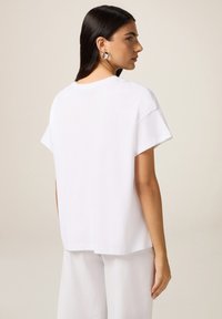 Witte katoenen t-shirt met korte mouwen, ontspannen pasvorm en een nekopening aan de achterkant. Gestyled met losse witte broek. Gladde, effen textuur.