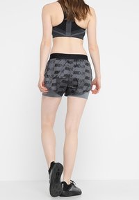 Nike Air-shorts i grått med svart logomönster, elastisk midja och en lätt design. Bärs med en svart sport-bh och sneakers.