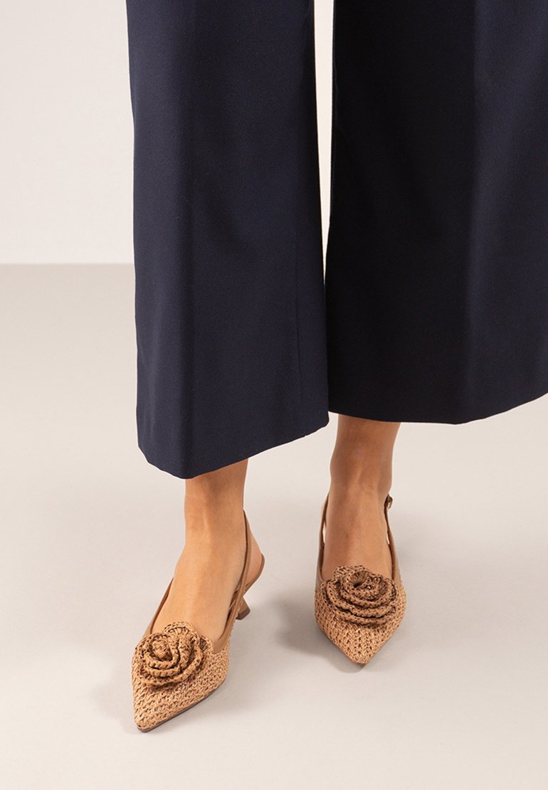 Zapatos slingback de punta en material trenzado color tostado, con un detalle de flor elevada en la punta. Los tacones bajos complementan un diseño texturizado.