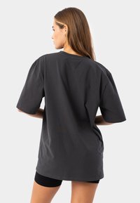 Oversized dark gray t-shirt in soft cotton, featuring short sleeves and a round neckline, with a smooth texture and minimal stitching details.