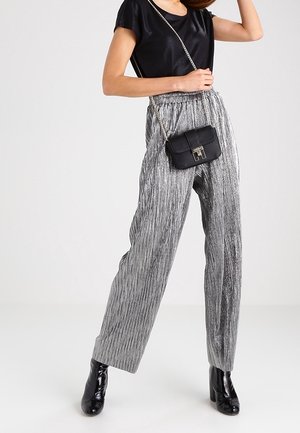 Metallisch silberne, plissierte weite Hosen kombiniert mit einem schwarzen kurzärmeligen Oberteil und einer kleinen schwarzen Umhängetasche, ergänzt durch schwarze Stiefeletten mit Absatz.