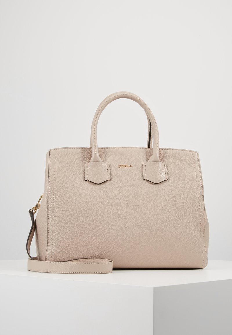 Beige läderhandväska med texturerad yta, två korta handtag och en avtagbar axelrem. Har minimala metalldetaljer och en strukturerad form.