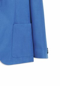 Manche et partie inférieure d’une veste de costume bleue montrant une poche plaquée rectangulaire et trois boutons noirs sur le poignet.