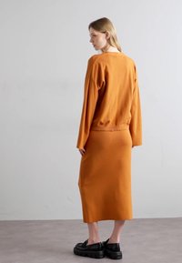 Ensemble en tricot de couleur rouille comprenant un pull et une jupe, avec des manches longues, une coupe décontractée et une texture côtelée. Associé à des chaussures à plateforme noires.