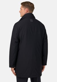 Abrigo negro aislante con un alto cuello, corte recto, costuras cosidas y una etiqueta de logo en la parte posterior. Presenta mangas largas y una textura suave.