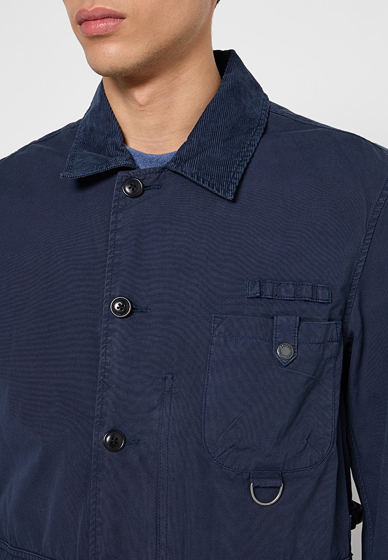 Giacca navy con colletto in velluto a coste, due tasche frontali, chiusura con bottoni e dettaglio in metallo a forma di anello. Texture liscia con design leggero.