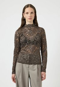 Langermet blondegenser i mørkegrå med blomsterprint og høyt hals. Kombinert med lysegrå bukser. Gjennomsiktig tekstur overalt.