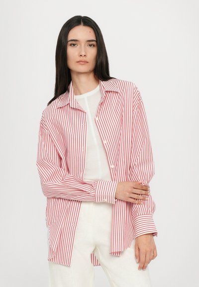 Rdeča in bela prugasta srajca z ovratnikom na gumb in dolgimi rokavi, z sproščenim fitom in mehkimi materiali. Oblačena čez belo majico.