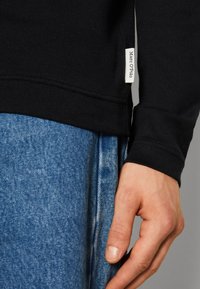 Czarny sweatshirt z ściągaczami, z bocznym rozcięciem i metką "Marc O'Polo". W połączeniu z jasnoniebieskimi dżinsami.