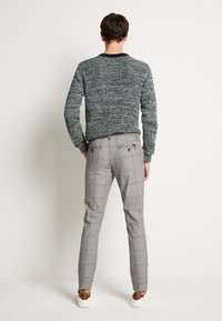 Pantalons gris à carreaux avec une coupe ajustée et deux poches arrière, associés à un pull texturé vert foncé, vus de derrière.