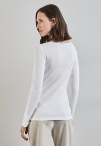Langarmweißes Baumwollshirt mit rundem Ausschnitt, glatter Textur und taillierter Passform, von hinten gezeigt.