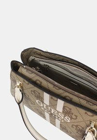 Bolso de mano abierto con un exterior estampado que presenta la marca "Guess". El interior muestra múltiples compartimentos y una sección con cremallera.