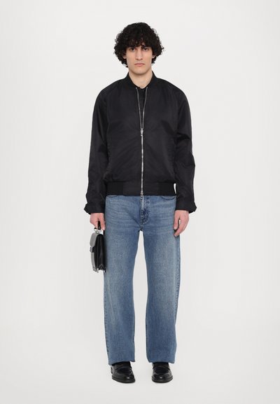 Zwarte bomberjack met een ritssluiting, ribbelmanchetten en contrasterend materiaal. Lichtblauwe rechte jeans met een gemiddelde wassing en een ontspannen pasvorm.