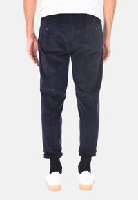 Pantaloni di velluto a coste blu navy con taglio affusolato, dotati di due tasche posteriori, texture a coste e orli arrotolati, abbinati a sneakers bianche.