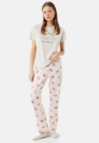 Lys grå t-shirt med teksten "GOD MORGEN KAFFE KLUB, HAV EN FANTASTISK DAG", parret med rosa pyjamasbukser med bagværksmønstre.