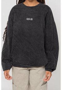 Černá oversize mikina z měkké látky s kulatým výstřihem a dlouhými rukávy. Na hrudi je bílý japonský nápis.