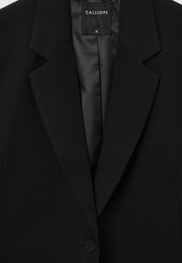 Blazer nero su misura con revers e chiusura a un bottone. Tessuto liscio con fodera interna in satin. Etichetta taglia: S.