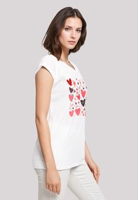 Weißes T-Shirt mit einem bunten Herz- und Stern- Grafikdesign, kurzen umgeschlagenen Ärmeln und lockerer Passform, aus weichem Baumwollmaterial gefertigt.