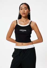 Czarny crop top z prążkowanej tekstury, białym wykończeniem i grafik�ą "Chicago" z przodu. Połączony z luźnymi czarnymi spodniami.