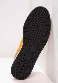 Chaussure de sport en daim orange avec semelle en caoutchouc noir, présentant un motif de semelle texturé pour une meilleure adhérence et des détails de semelle intermédiaire blanche.