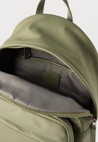 Ανοιχτό χακί πράσινο σακίδιο πλάτης που δείχνει το επενδυμένο διαμέρισμα για φορητό υπολογιστή και την εσωτερική τσέπη με ετικέτα Calvin Klein.