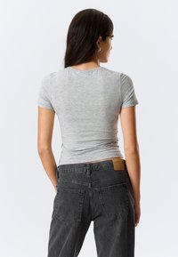 Kurzärmeliges graues T-Shirt aus weichem, dehnbarem Stoff, kombiniert mit hoch taillierten dunkelgrauen Jeans mit Gesäßtaschen und einem Lederetikett.