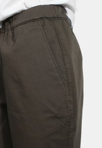 Pantaloni verde oliva scuro, realizzati in cotone morbido, con vita elastica e tasche laterali; superficie liscia con poche pieghe.