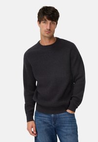 Mørkegrå, ribstrikket sweater med rund hals, lange ærmer og en afslappet pasform, kombineret med blå denimjeans.