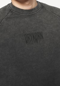 Ciemnoszara bluza z wykończeniem o fakturze, okrągłym dekoltem i nadrukowanym czarnym logo "DRYKORN". Posiada raglanowe rękawy i prążkowany kołnierz.