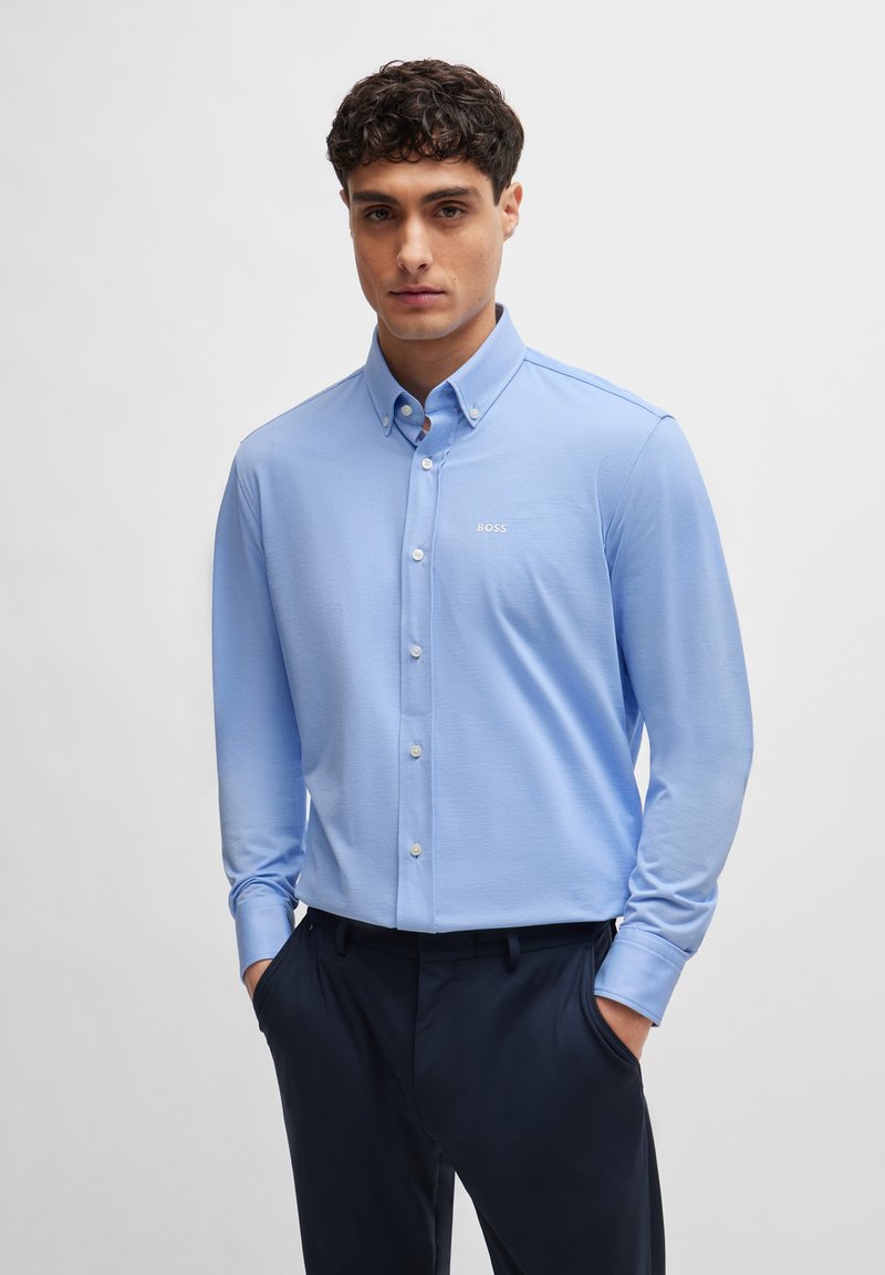 Light blue long-sleeve shirt with a button-down collar, featuring a small white embroidered logo. Smooth texture and fitted design.