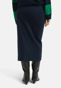 Marineblaue Midi-Rock mit glatter Textur und figurbetontem Schnitt. Kombiniert mit glänzenden schwarzen, kniehohen Stiefeln im Krokodil-Muster.