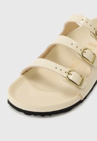 Beige sandaler med tre justerbare stropper og gullfargede spenner. Glatt overflate, polstret fotseng og svart teksturert såle.