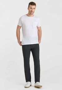 Wit katoenen T-shirt met korte mouwen, voorzien van een klein borstzakje; gecombineerd met donkergrijze broek en witte sneakers. Eenvoudig, klassiek design.