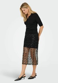 Melns īss piedurkņu tops kopā ar melnu vidēja garuma svārku ar spīdīgiem fliteriem, caurspīdīgu virsmu un dekoratīviem rakstiem, papildināts ar melniem augstpapēžu apaviem.