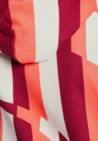 Felpa colorata con strisce alternate in corallo, rosso e bianco. Il materiale sembra morbido con una texture liscia.