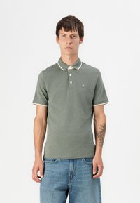Groene polo met een gestructureerde stof, contrasterende witte kraag en mouwafwerking, een twee-knopen sluiting en een klein logo op de borst.