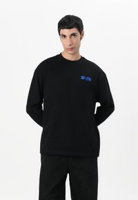 Black long-sleeve t-shirt featuring a blue embroidered logo on the left chest. The fabric has a smooth texture and relaxed fit.
