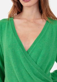 Pull vert léger en maille avec un profond décolleté en V et un design cache-cœur. Texture douce avec des accents côtelés au niveau de l'encolure et des poignets.