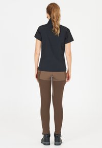 Top nero a maniche corte con colletto alto, abbinato a pantaloni aderenti marroni con pannelli a contrasto e zip. Calzature nere completano il look.