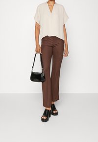 Ljus beige kortärmad topp, bruna ribbade byxor, svart handväska och svarta plattformssandaler med öppna tår. Tydliga linjer och modern design.