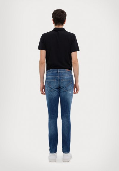 Tummanpuhuva polo-paita, siniset kapeat farkut, joissa on hieno kulutus ja takataskut, yhdistettyinä valkoisiin tennareihin, nähtynä takaa.