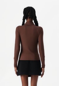 Brown ribbed long-sleeve top with a high collar, paired with a black skirt. The top features a fitted design and textured fabric.