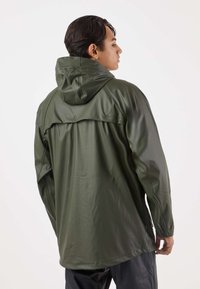 Olijfgroene, waterdichte jas met capuchon. Gladde, glanzende textuur, voorzien van een geknoopte achterklep en elastische manchetten. Getailleerde pasvorm met een lange silhouet.