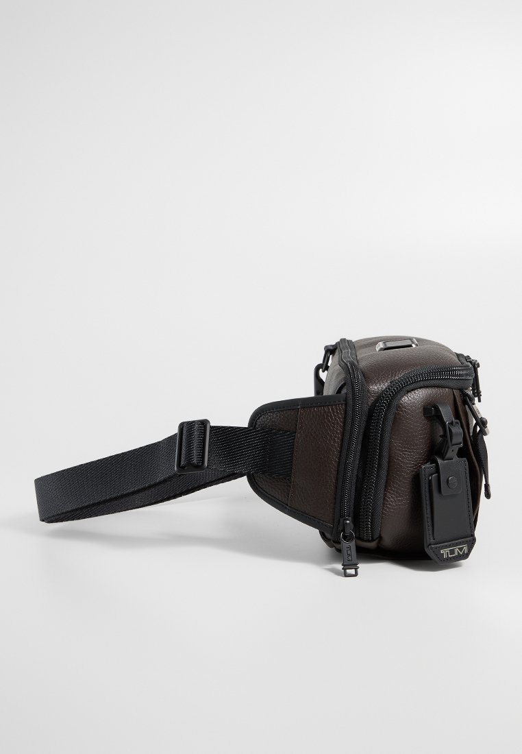 Braune Leder-Schultertasche mit schwarzem Tragegurt, Reißverschlussfächern und einem abnehmbaren Anhänger. Verfügt über eine strukturierte Oberfläche und ein kompaktes Design.