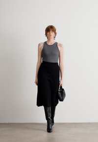 Gray sleeveless top paired with a mid-length black skirt, black thigh-high boots, and a small textured black handbag. Simple, modern aesthetic.